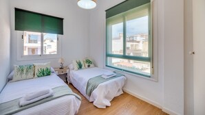 Une chambre avec deux lits, une fenêtre donnant sur des immeubles, une table de chevet avec une lampe et un luminaire suspendu.
