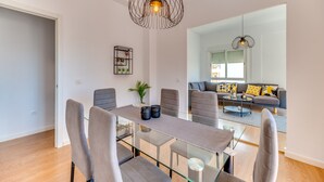 Un salon moderne avec une table à manger en verre, des canapés gris et une grande fenêtre.