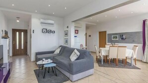 A modern living room with a grey sofa, a small round table, and a dining area with a white table and chairs. - Beautiful home in Koromacno-Brovinje (Koromacno-Brovinje)