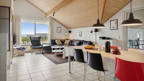 Ein modernes Wohnzimmer mit Holzboden, einer Couch, einem Esstisch mit Stühlen und Blick ins Freie.