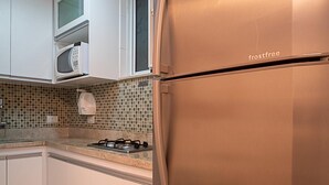 Eine Küche mit weißen Schränken, einem Edelstahlkühlschrank, einer Mikrowelle und einer gefliesten Spritzschutzwand.