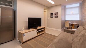 Ein modernes Wohnzimmer mit Flachbildfernseher, eingebautem Backofen, Essbereich mit Tisch und Stühlen sowie einer Couch.