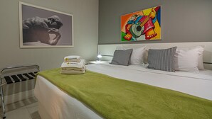 Ein Hotelzimmer mit einem ordentlich bezogenen Bett, einem grünen Handtuch, einem Bild an der Wand und einem Handtuchhalter.