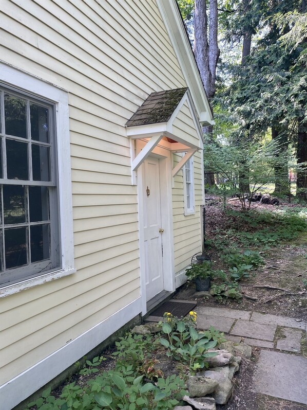 Una casa con puerta y ventana blancas, rodeada de un jardín con plantas y un sendero de piedra.