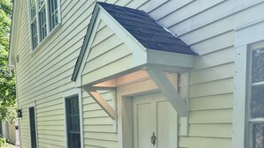 Ein Haus mit weißer Tür, einer kleinen Veranda und einem Steinweg, der zum Eingang führt.