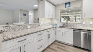 A kitchen with white cabinets, granite countertops, a stainless steel dishwasher, and a window with a view. - Pool 5BR/3BA Launchpad (Titusville)