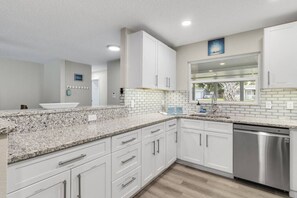 A kitchen with white cabinets, granite countertops, a stainless steel dishwasher, and a window with a view.