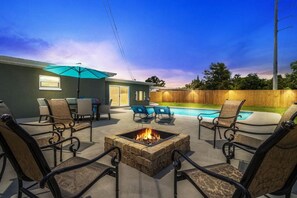 A backyard with a fire pit, outdoor seating, a pool, and a wooden fence.
