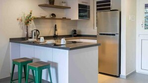 A modern kitchen with a stainless steel refrigerator, a built-in oven, and a sink. There are two green stools and a vase with flowers on the counter. - CASA ARTE- Modern Apt+ Car option & Pool (Willemstad)