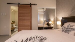 A bedroom with a bed, a wooden sliding door, a mirror, and a nightstand with a lamp. - CASA ARTE- Modern Apt+ Car option & Pool (Willemstad)