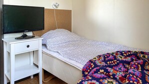 Et soveværelse med en seng, et fjernsyn på et hvidt natbord og en lampe på væggen.