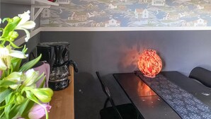 Et værelse med tapet med mønster, en kaffemaskine, en vase med blomster og et bord.