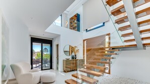 A modern interior with a glass staircase, a seating area with a sofa and ottoman, and a view of the outdoors. - All About Playas Andaluzas Villa (Marbella)