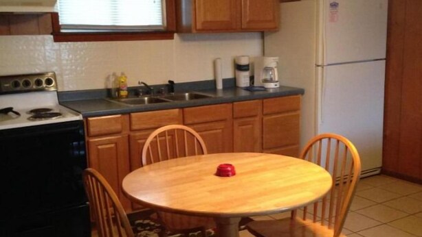 A kitchen with wooden cabinets, a stove, a sink, and a refrigerator. There is a round wooden table with four chairs. - Two-Bedroom Apartment (Robbinsville)