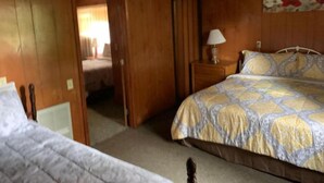A wooden-paneled room with a bed, a nightstand, and a door leading to another room. - Two-Bedroom Apartment (Robbinsville)