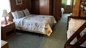 A wooden room with a bed, a nightstand, a lamp, a wardrobe, and a mirror. - Two-Bedroom Apartment (Robbinsville)