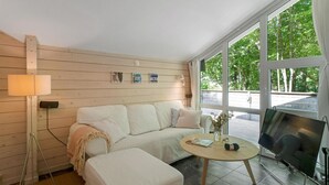 Una habitación acogedora con un sofá blanco, una mesita redonda pequeña, una lámpara y un televisor.