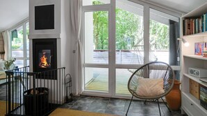 Una habitación con chimenea, ventanas amplias, una silla de mimbre y una estantería.