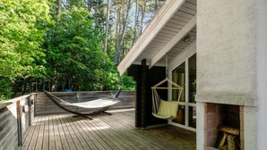 Terraza de madera con una hamaca y un sillón colgante, con vistas a una zona boscosa.