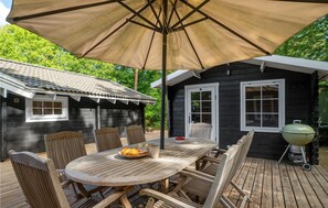 Une terrasse extérieure en bois avec une table ronde et des chaises, un grand parasol et un barbecue.
