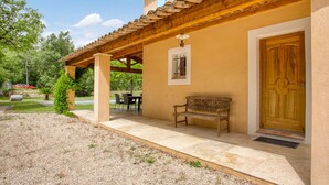 Une terrasse couverte avec un banc, une porte en bois et une petite fenêtre dotée d’un grillage métallique.