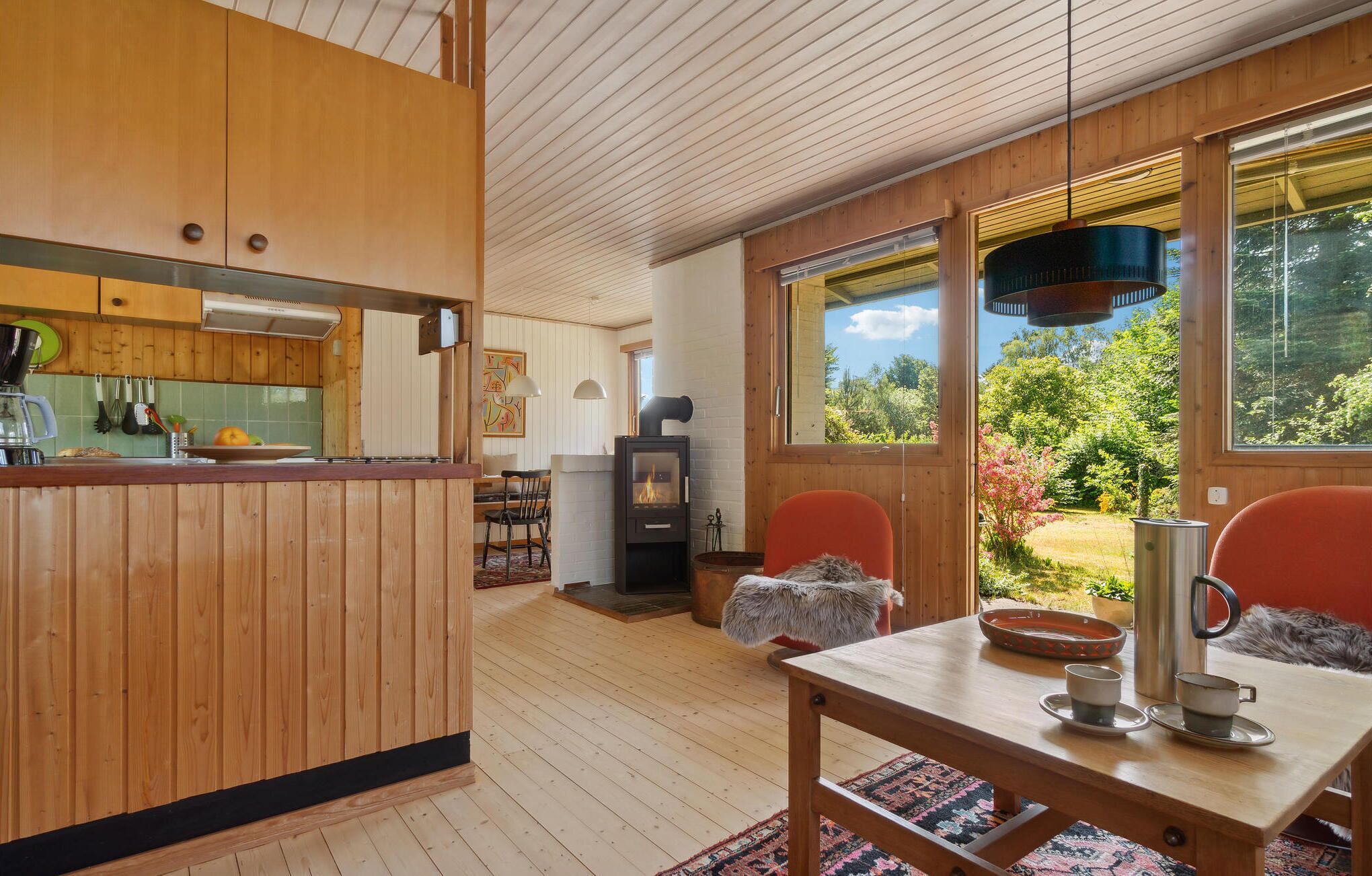 Interior acogedor de una cabaña con detalles de madera, una zona de comedor con mesa y sillas, una cocina con estufa y ventanas amplias que ofrecen vistas del exterior.
