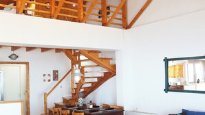 A spacious living area with a high wooden ceiling, a staircase, and a dining area.