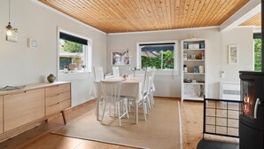 A cozy kitchen with a wooden ceiling, white cabinets, a dining table with chairs, and a black stove. - Amazing home in Jægerspris with WiFi (Jægerspris)