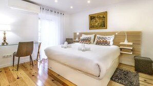 A modern hotel room with a large bed, a desk, a chair, and a painting on the wall. - GuestReady - Exclusive Apartment at São Bento (Lisbon)