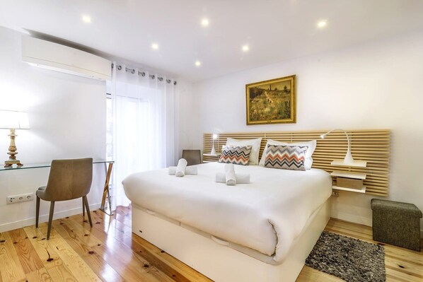 A modern hotel room with a large bed, a desk, a chair, and a painting on the wall.