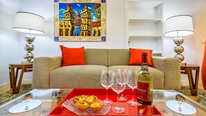 A living room with a sofa, red cushions, a glass coffee table with wine glasses, a bottle, and a tray with pastries. - GuestReady - Exclusive Apartment at São Bento (Lisbon)