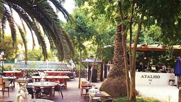 An outdoor dining area with tables and chairs, a fountain, and a sign reading "ATALHO." - GuestReady - Exclusive Apartment at São Bento (Lisbon)