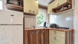 A compact kitchen with a built-in stove, a microwave, and a refrigerator. There is a window providing natural light and a view of greenery outside. - 3 bedroom beautiful (sta)caravan in Sete (Sete)