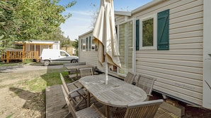 A mobile home with a patio area featuring a wooden table and chairs, an umbrella, and a white van parked nearby. - 3 bedroom beautiful (sta)caravan in Sete (Sete)