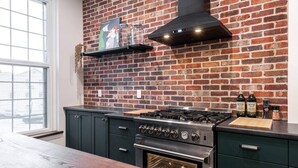 A kitchen with a brick wall, a gas stove, a built-in oven, and a window. - Juno Lofts: Memories of Gastown (Stratford)