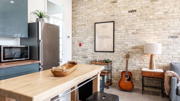 Eine Küche mit einer Holzausziehtheke, einer Mikrowelle, einem Kühlschrank, einer Gitarre und einem gerahmten Zitat an der Wand.