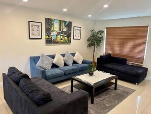 Relax in this stylish living room with a sofa, armchair, and coffee table, surrounded by artwork and a lush potted plant.