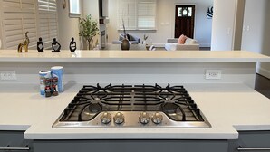 Una cocina moderna con estufa de acero inoxidable, encimera blanca y una zona de comedor al fondo.