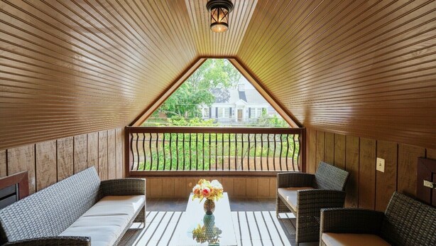 Una habitación acogedora con paneles de madera, un balcón con barandilla y una mesa con un florero.