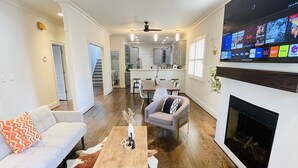 Una sala moderna con un sofá, una mesa de centro y una chimenea. Se observa una cocina al fondo, con un televisor montado sobre la chimenea.