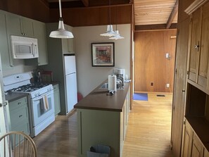 Kitchen area with central island, stove, sink, and microwave, featuring light-colored cabinets and a wooden floor.