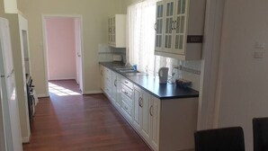 A kitchen with white cabinets, a black countertop, and a dining area with a table and chairs. - "Roseneath" Private room with en-suite, Rm 3 (Northam)