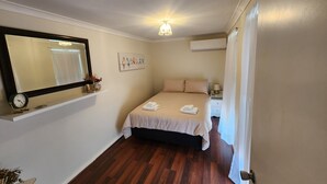 A bedroom with a bed, a nightstand, a wall-mounted air conditioner, a ceiling light, a clock, and a shelf with decorative items. - "Roseneath" Private room with en-suite, Rm 3 (Northam)