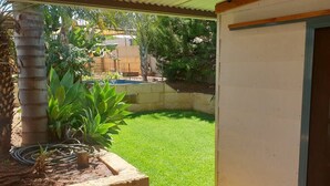 A backyard with a well-maintained lawn, a palm tree, and a concrete planter with plants. - "Roseneath" Private room with en-suite, Rm 3 (Northam)