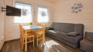 Ein gemütliches Blockhauss-Interieur mit einem Holzespeisetisch, vier Stühlen, einem grauen Sofa und einem Wand-Fernseher.