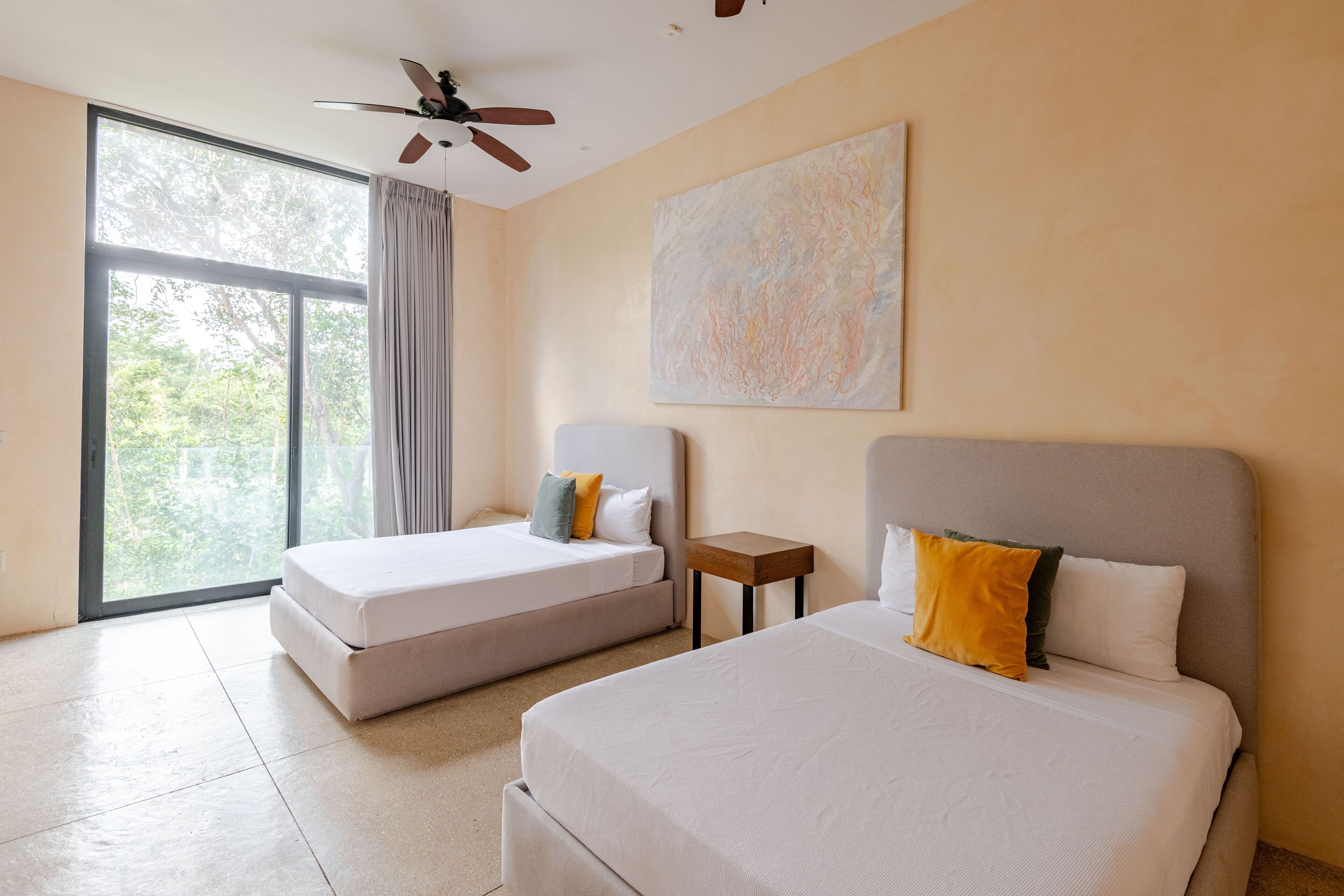 Une chambre d’hôtel avec deux lits, un ventilateur de plafond, une grande fenêtre et un tableau au mur.
