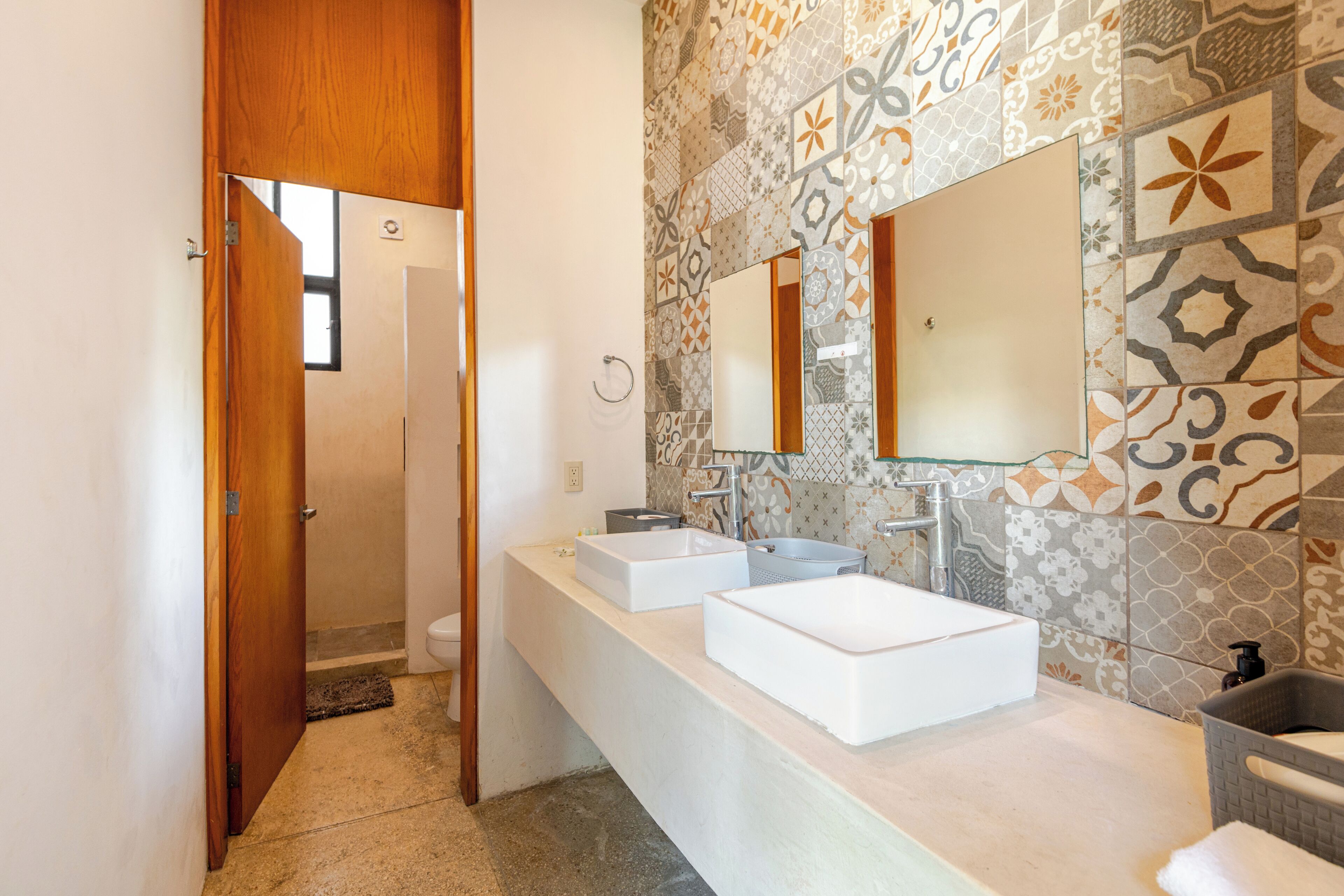 Um banheiro com pia branca, espelho e azulejos estampados nas paredes.