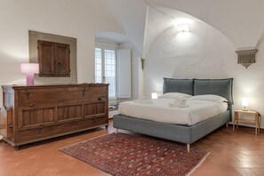 A bedroom with a large bed, a wooden dresser, a red patterned rug, and a white ceiling with a skylight.