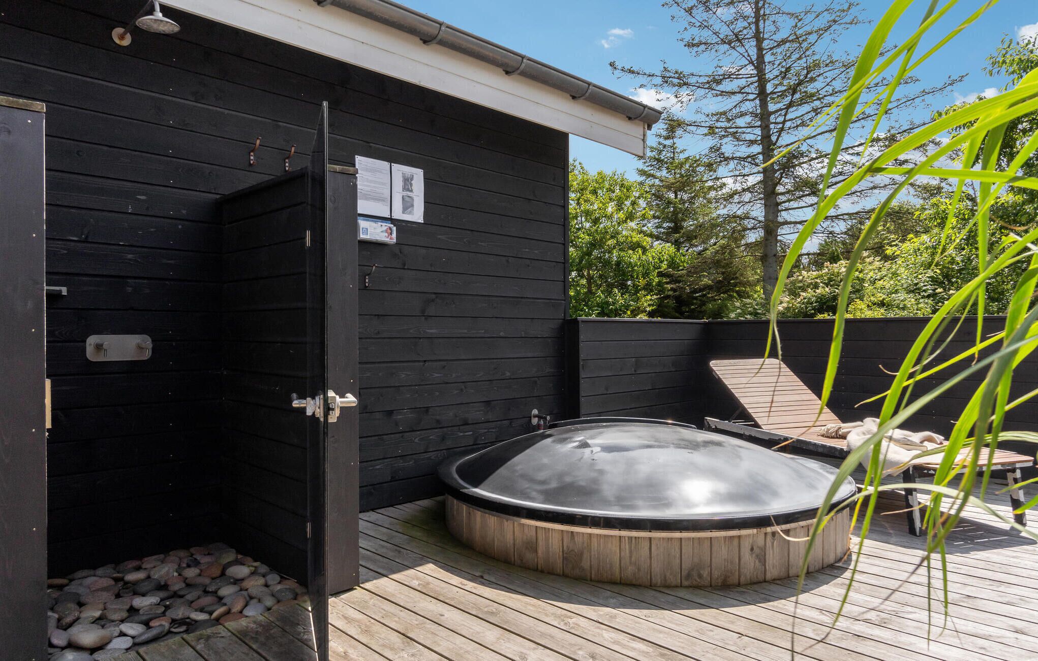 A hot tub on a wooden deck with a black wall and a wooden fence in the background.