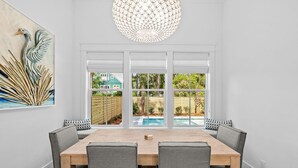 Un'area pranzo con un tavolo in legno e sedie grigie, ampie finestre vista piscina e vegetazione, e un elemento decorativo a parete.